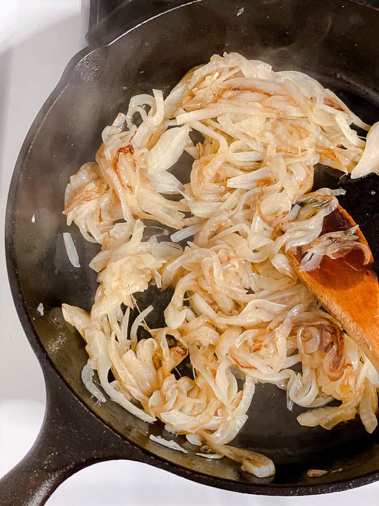 a wooden spoon stirring caramelized onions in a large black skillet.