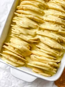 sliced potatoes in a casserole dish with a cream sauce poured on top.