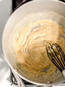 whisking a roux in a large grey pot.