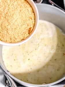 pouring nutritional yeast into a cream sauce.