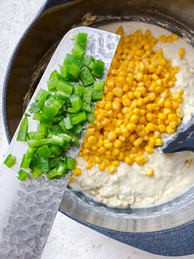 holding diced jalapenos over cornbread batter in a bowl.