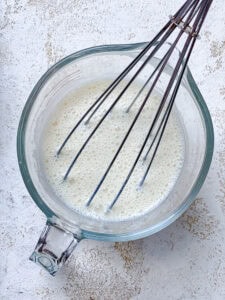 whisking wet ingredients for vegan jalapeno cornbread in a glass measuring cup.