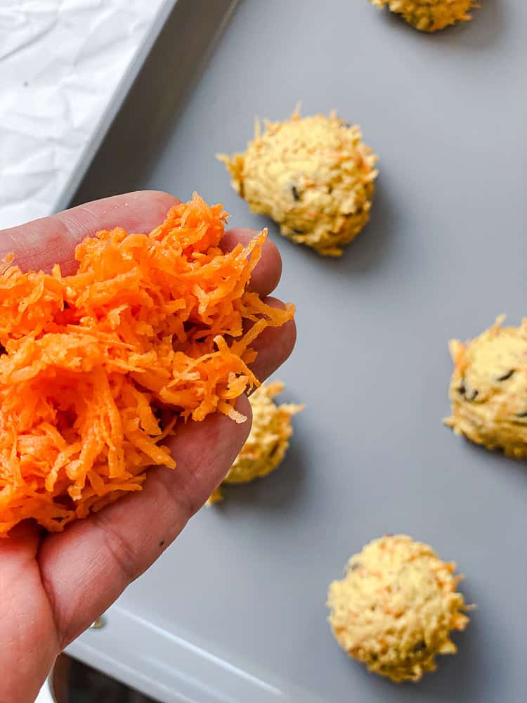 Sprinkling grated sweet potato over cookie dough balls on a baking sheet.