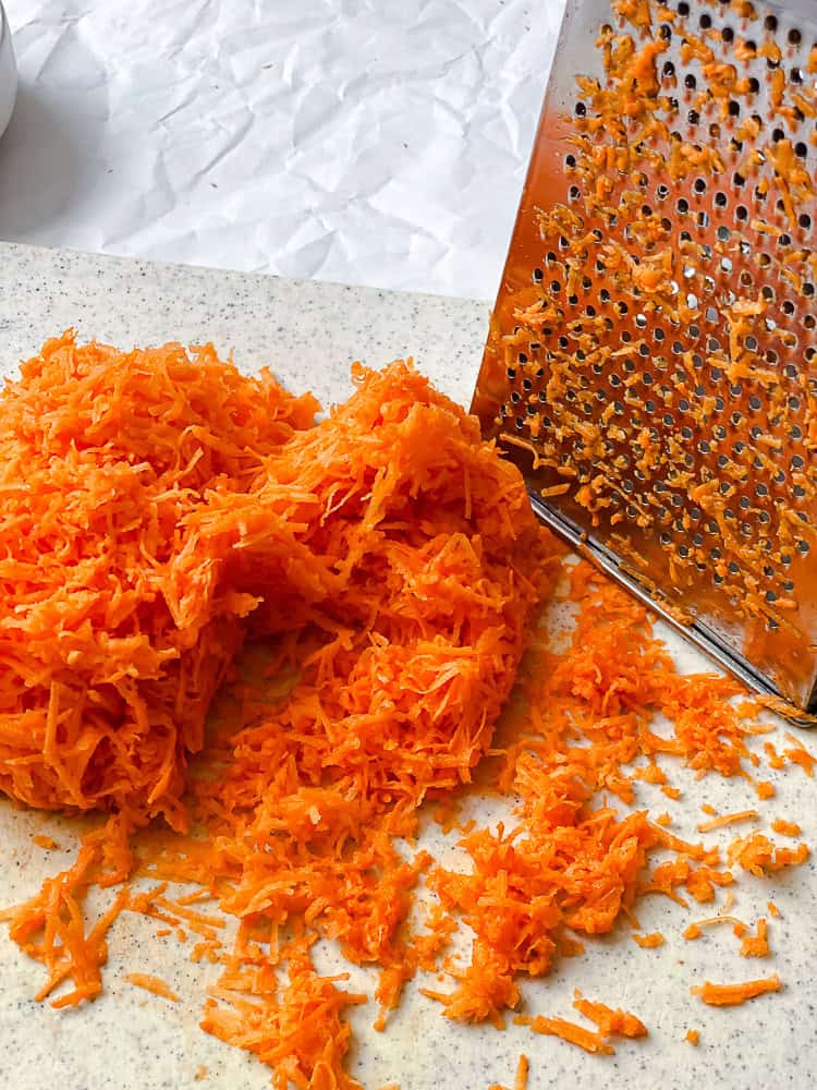 Finely grated sweet potato next to a box grater.