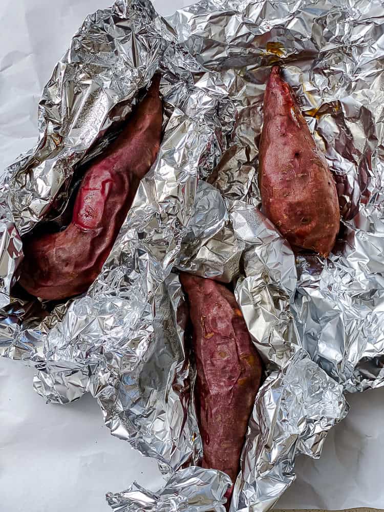 3 roasted sweet potatoes surrounded by foil.