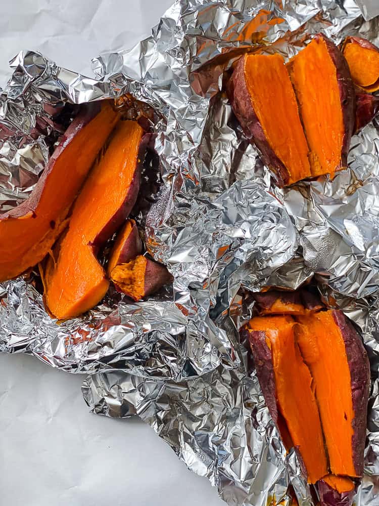 3 halved roasted sweet potatoes surrounded by foil.