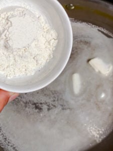 Flour being whisked into melted vegan butter in a pan.