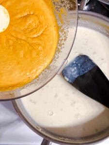 Butternut squash sauce being whisked into the roux in a pan.