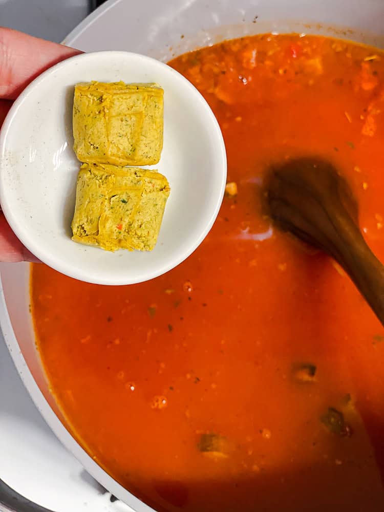 2 bouillon cubes being held above a pot of vegan lasagna soup.