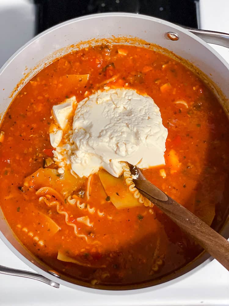 using a wooden spoon to stir silken tofu into a pot of vegan lasagna soup.