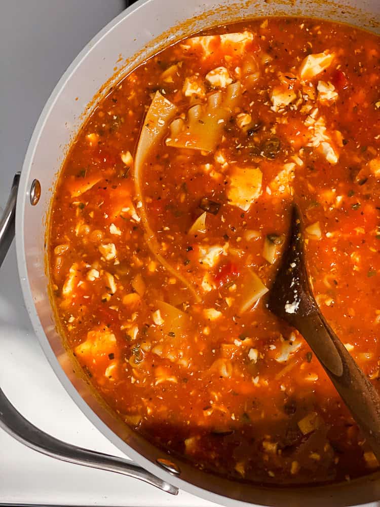 a wooden spoon stirring a pot of vegan lasagna soup.