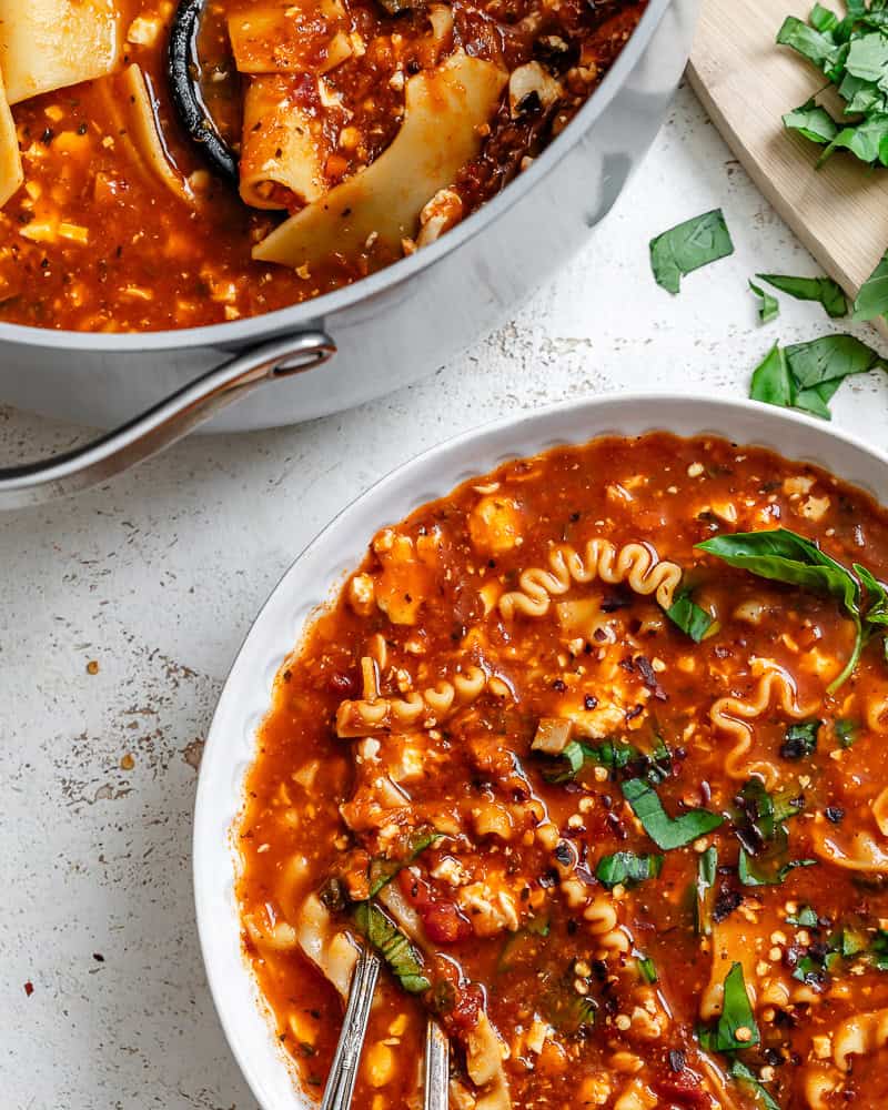 a bowl of vegan lasagna soup next to a large pot.