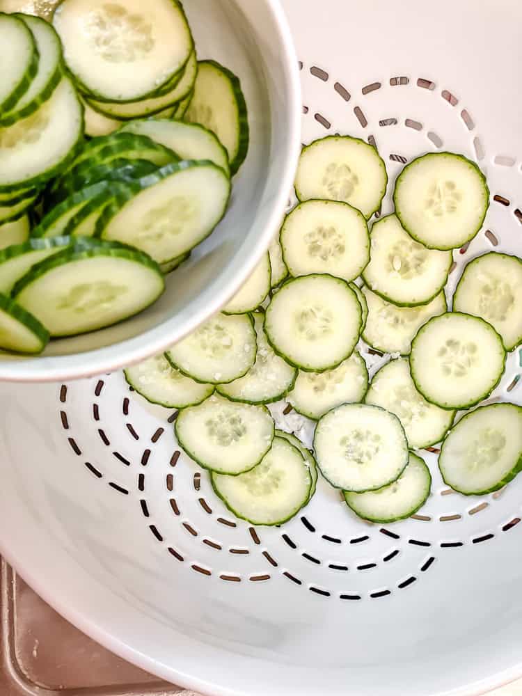 sliced cucumbers in a white colander.