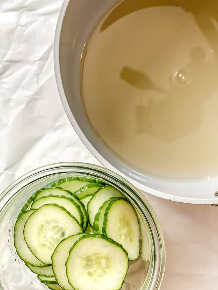 sliced cucumbers in a glass dish next to a saucepan.