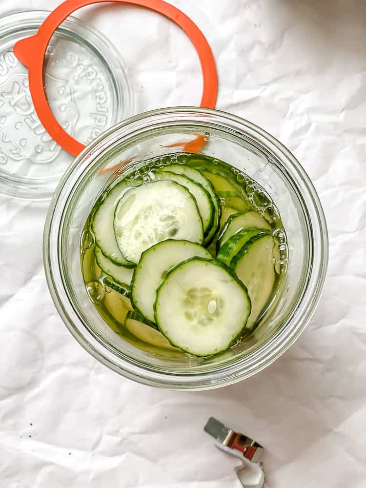 sliced cucumbers and marinade in a glass jar.