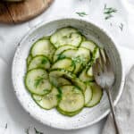 cucumber dill salad in a white bowl with a fork.