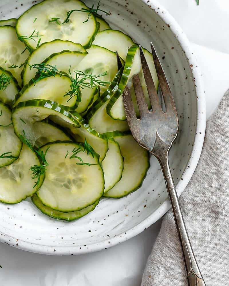 cucumber dill salad in a white bowl with a fork.