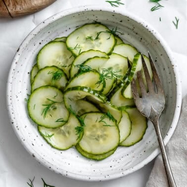 cucumber dill salad in a white bowl with a fork.