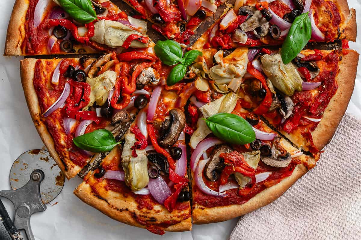 completed Easy Vegan Pizza Dough with pizza toppings on top on white surface