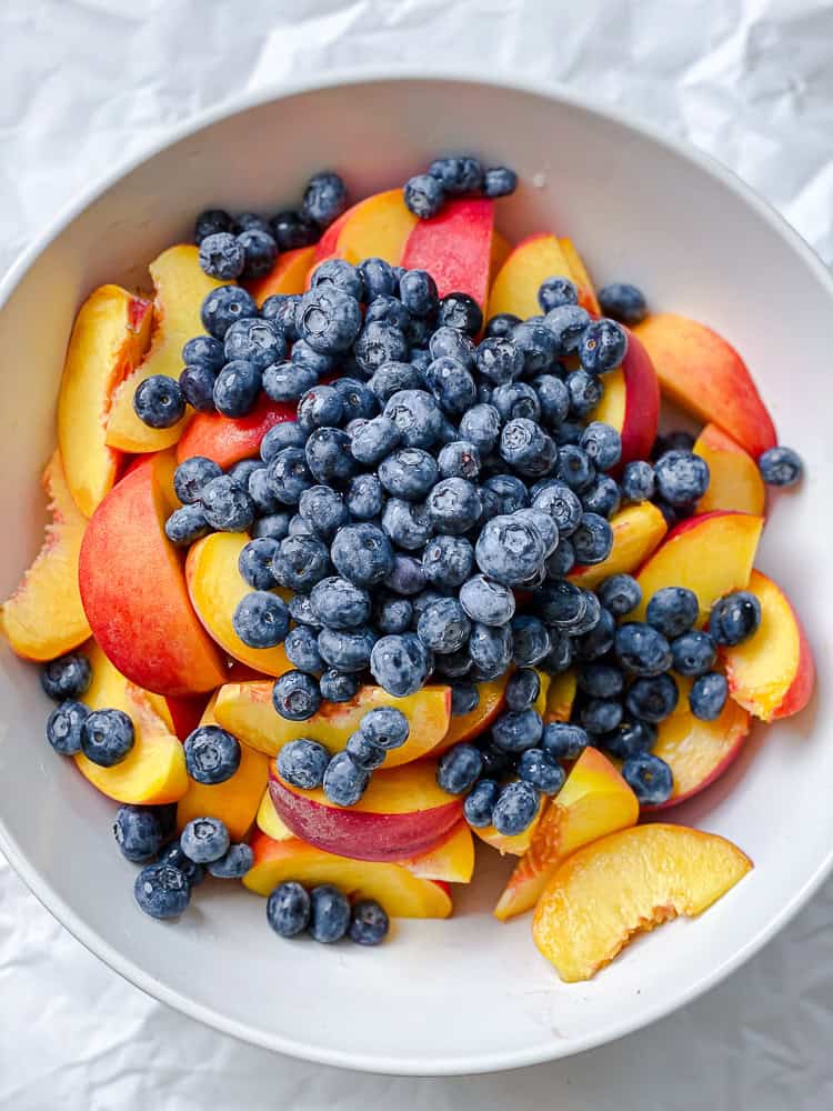 process shot showing blueberries added to bowl of peaches