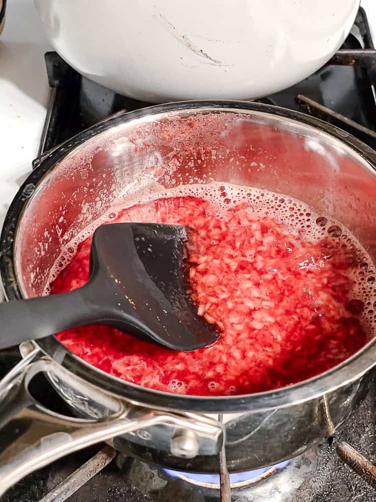 using a black spatula to stir raspberry sauce in a saucepan.
