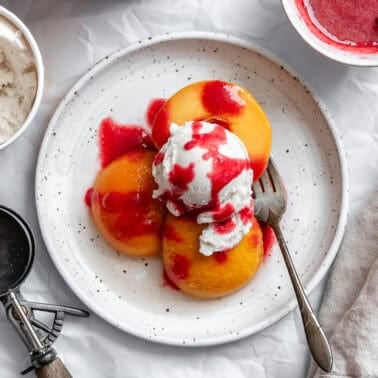 poached peaches topped with raspberry sauce and ice cream on a plate.
