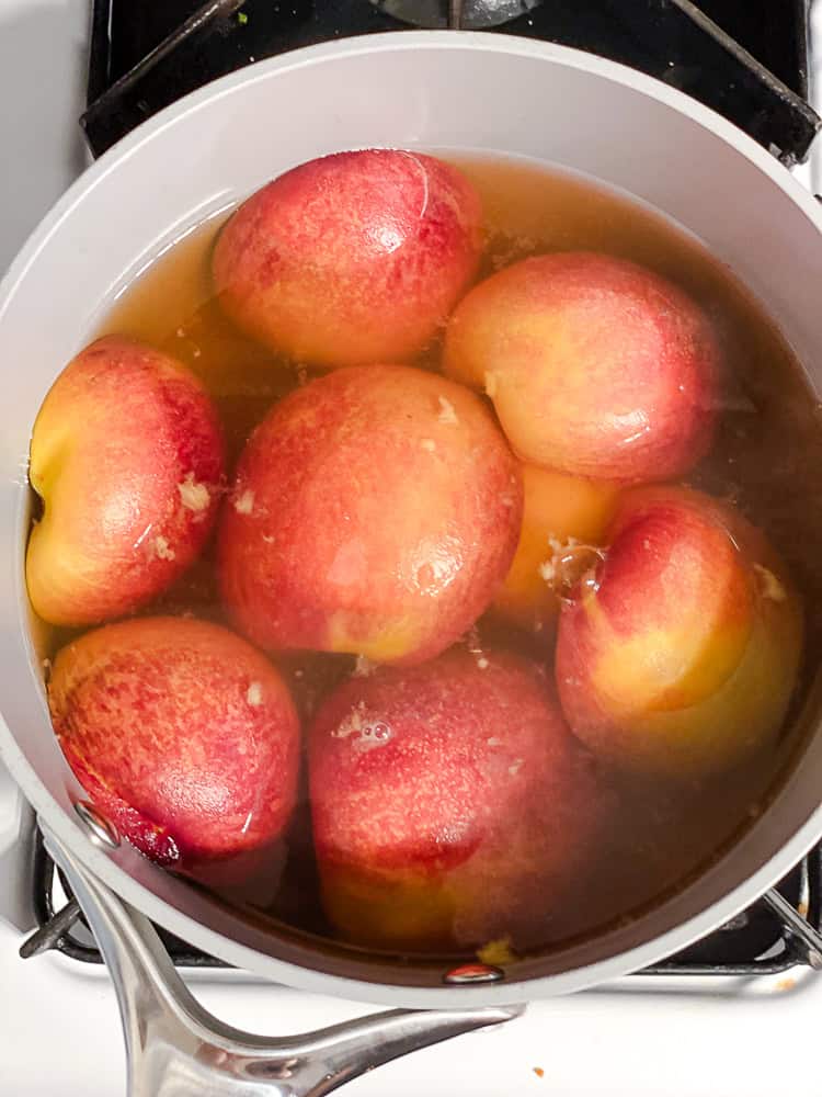 poaching peaches in a saucepan filled with simple syrup.