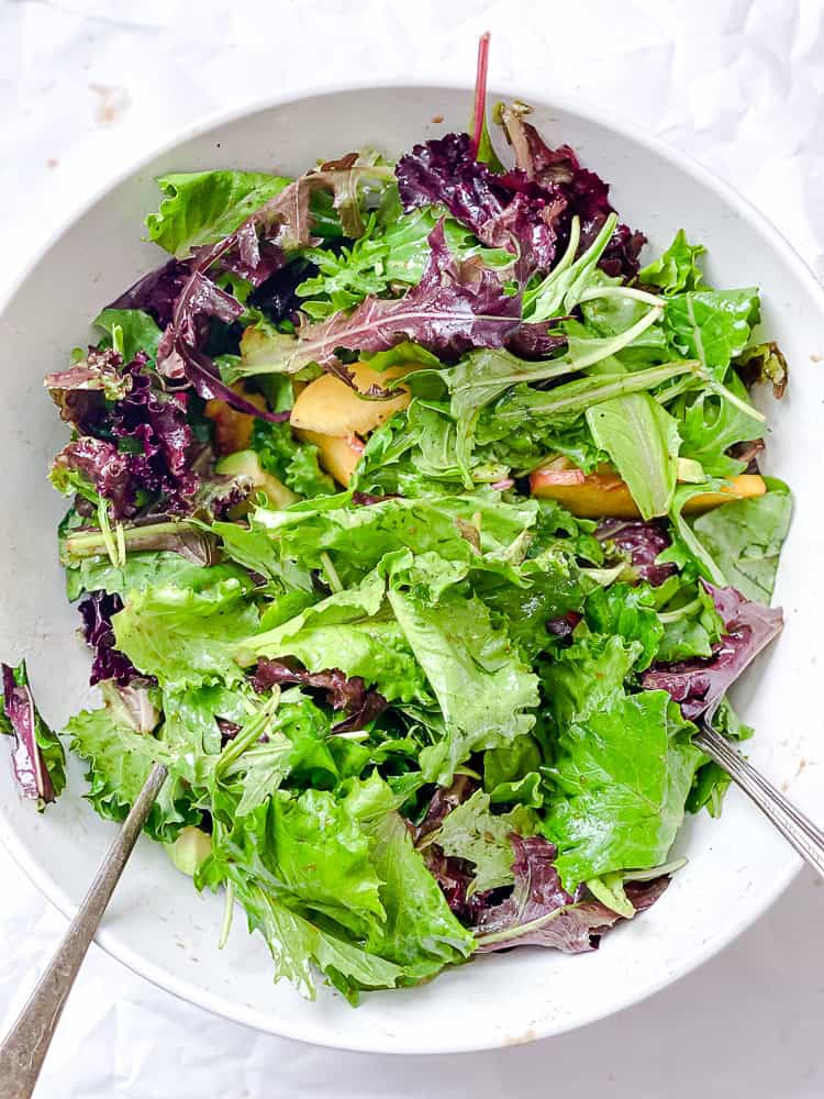 salad greens and peach slices in a large white bowl.