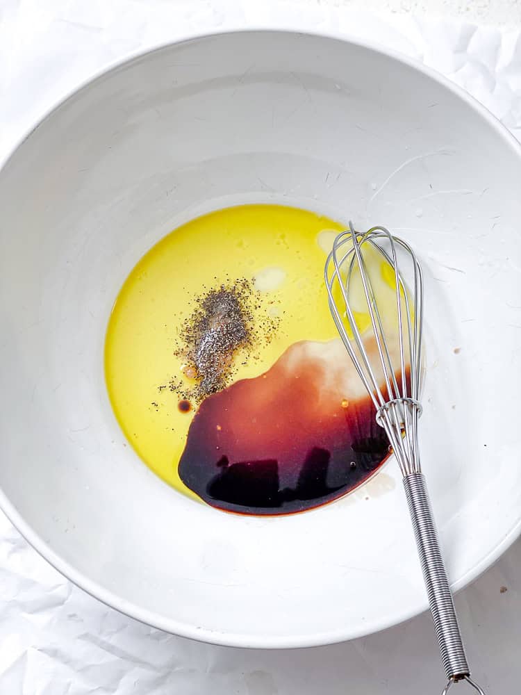 whisking the dressing for a peach salad in a large white bowl.