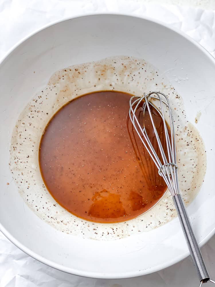 whisking the dressing for a peach salad in a large white bowl.