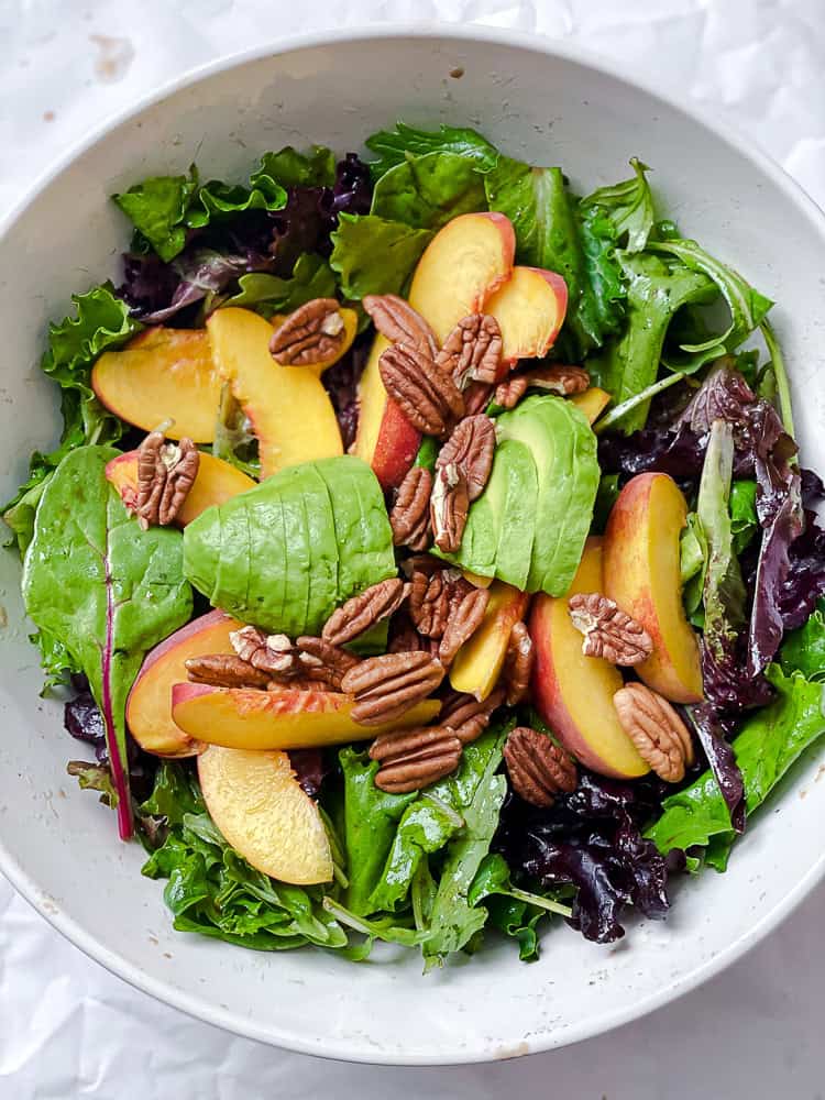 salad greens, peach slices, and pecans in a large white bowl.