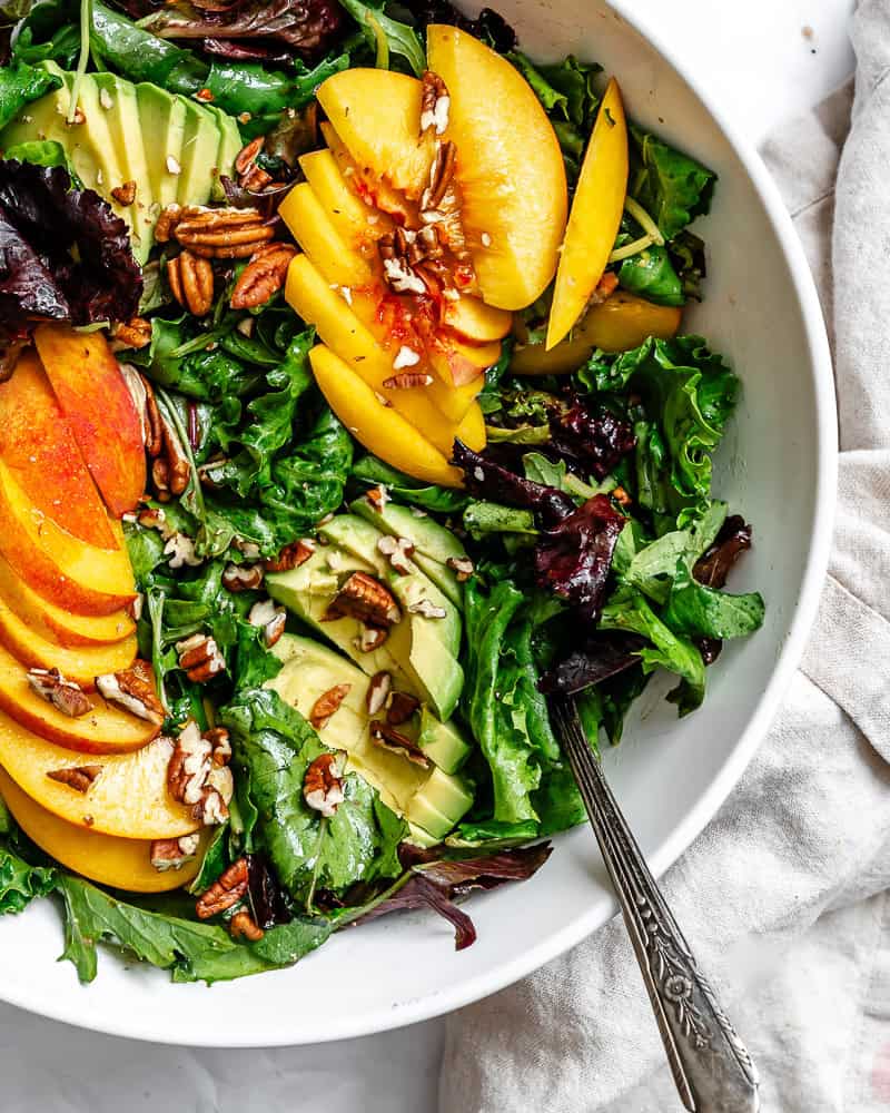 close up on a peach salad in a large white bowl.