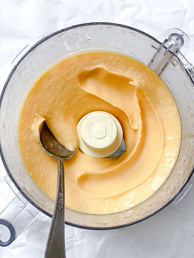 using a spoon to scoop blended peach sorbet in a food processor.