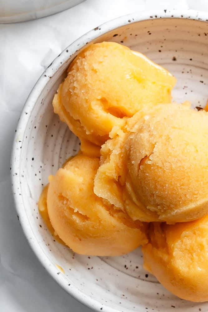 close up on scoops of peach sorbet in a white bowl.