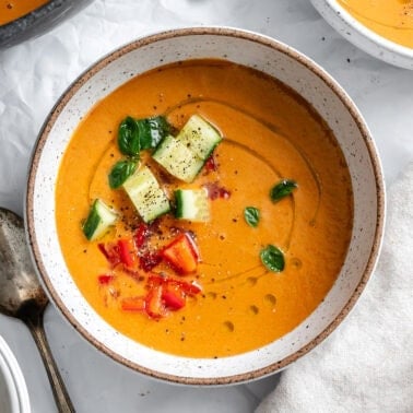 a bowl of Watermelon Gazpacho with chopped cucumbers, basil, and red peppers on top.