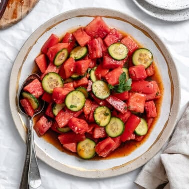 a dressed Watermelon Tomato Salad on a white plate with a spoon on the side.