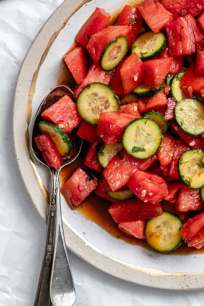 a dressed Watermelon Tomato Salad on a white plate with a spoon on the side.