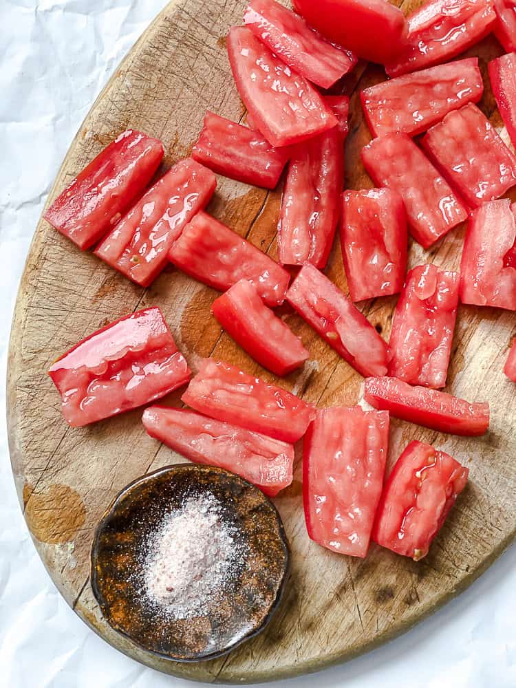 sliced tomatoes and a bowl of salt on a wood cutting board.