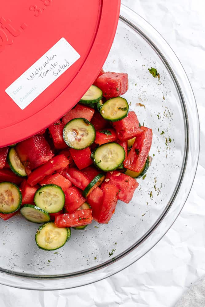 a Watermelon Tomato Salad in a large glass bowl with a red lid on top.