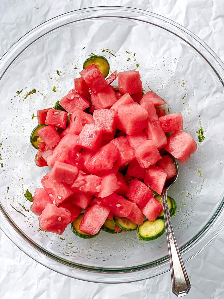 using a spoon to toss a watermelon tomato salad together.