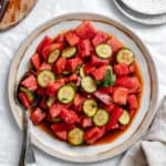 a dressed Watermelon Tomato Salad on a white plate with a spoon on the side.