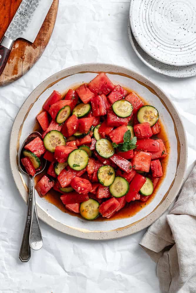 a dressed Watermelon Tomato Salad on a white plate with a spoon on the side.