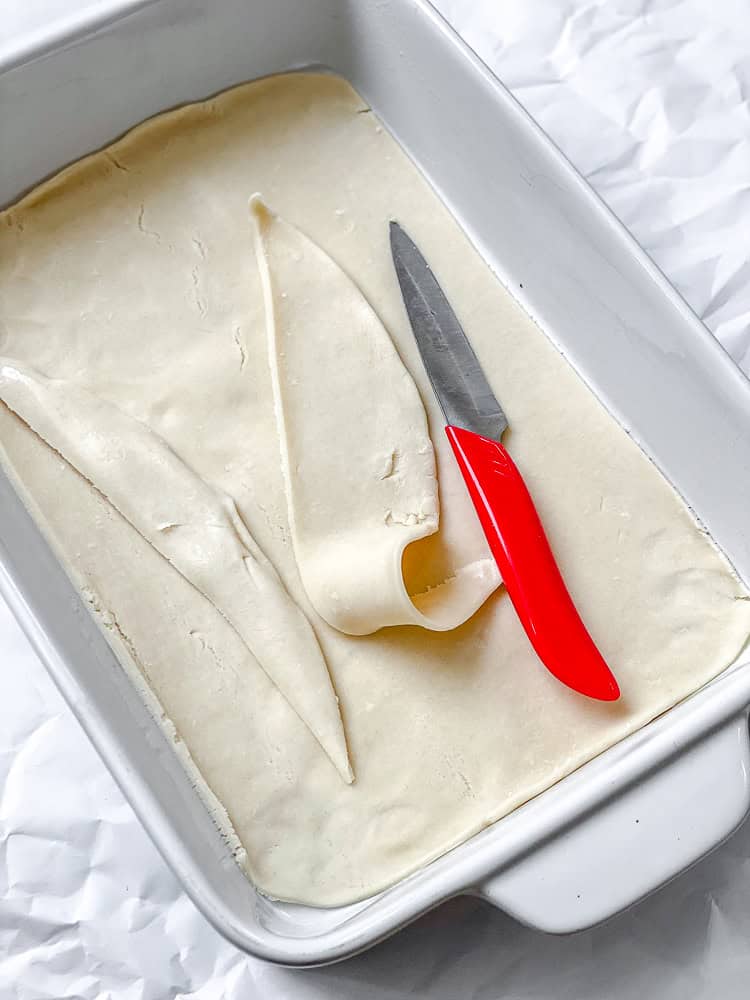 Trimming the extra dough from a vegan pie crust pressed into an empty 9x13 baking dish.