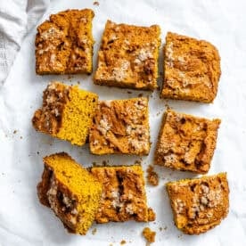 Squares of pumpkin coffee cake with a crumbly streusel topping on white parchment paper.