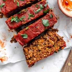 Slices of lentil loaf topped with a red glaze and chopped parsley on parchment paper.