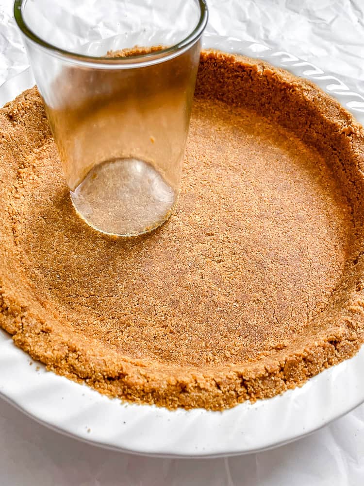 Process shot showing using a glass to flatten out graham cracker mixture in pan.