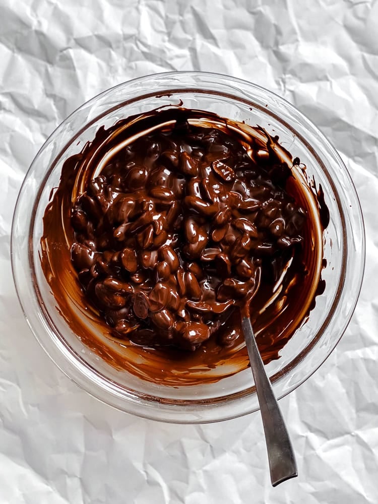 Process shot showing peanuts and vegan chocolate in a bowl.