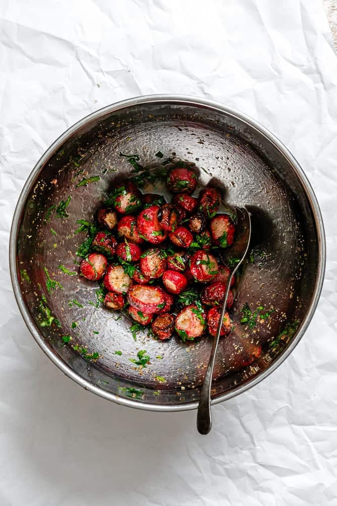 Process shot showing seasonings mixed with radishes on plate.
