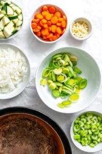 Process shot showing veggies cut up in separate bowls on white surface.
