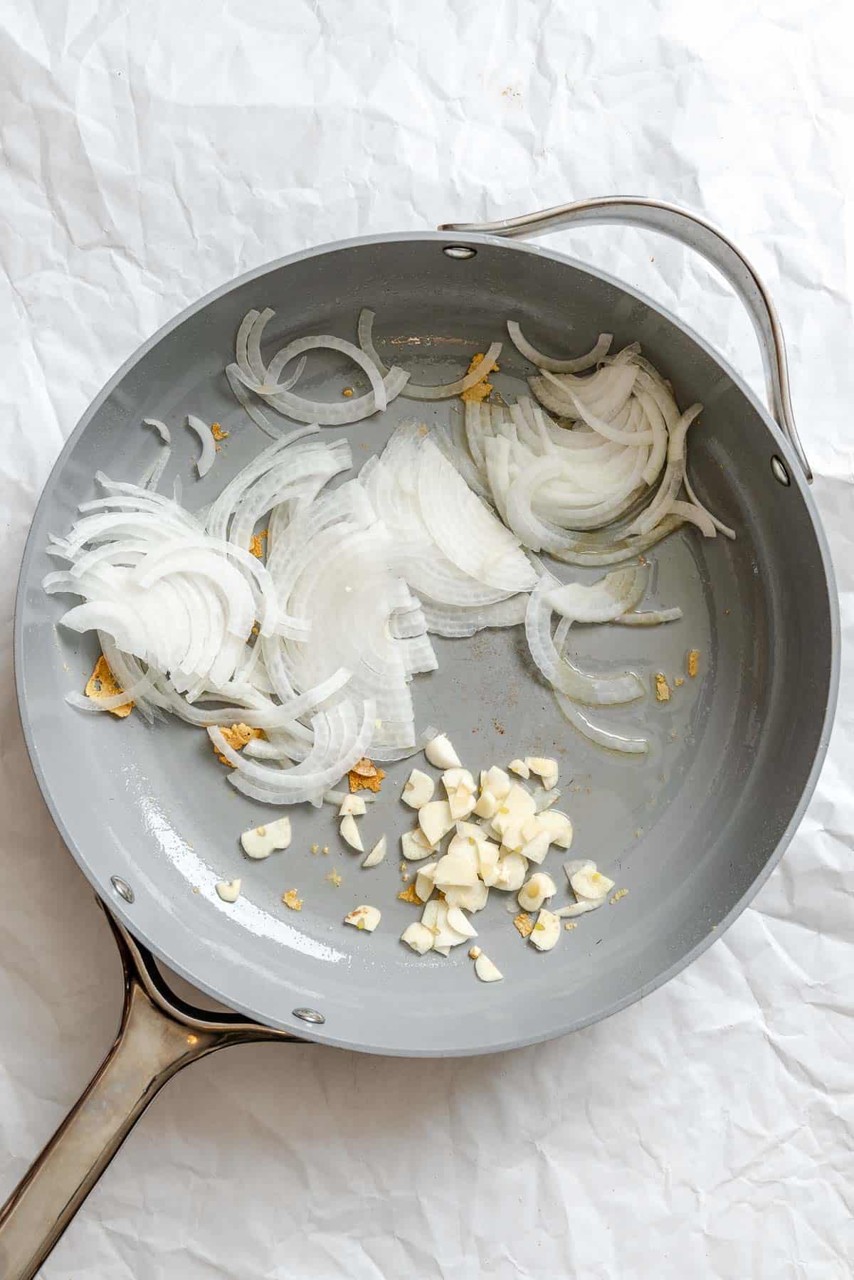 Process shot showing onions and garlic cooking in pan.